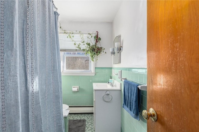 bathroom with toilet, a wainscoted wall, vanity, a baseboard heating unit, and tile walls