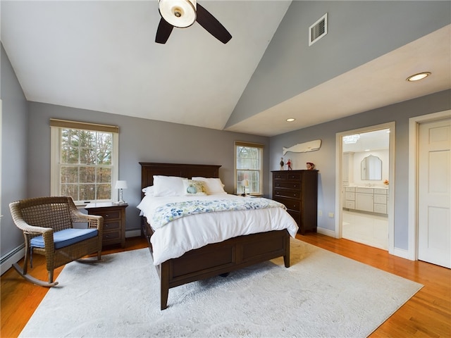 bedroom featuring lofted ceiling, light hardwood / wood-style flooring, ceiling fan, a baseboard heating unit, and connected bathroom