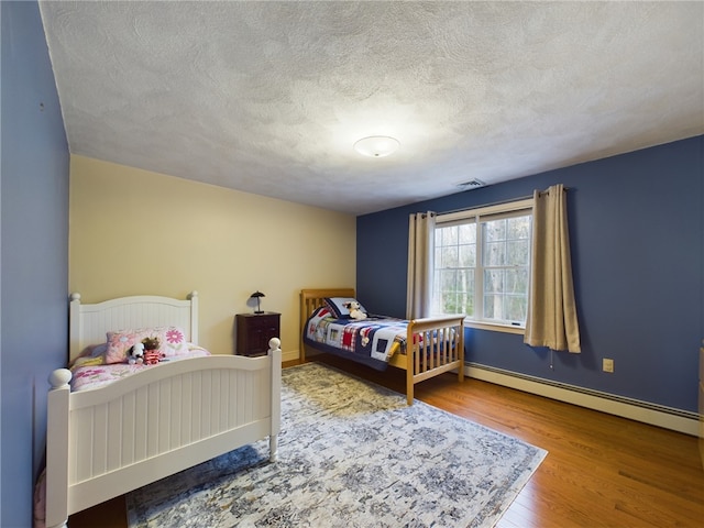 bedroom featuring wood-type flooring, a textured ceiling, and a baseboard heating unit