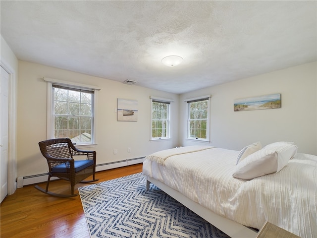 bedroom featuring hardwood / wood-style flooring, a baseboard heating unit, and a textured ceiling