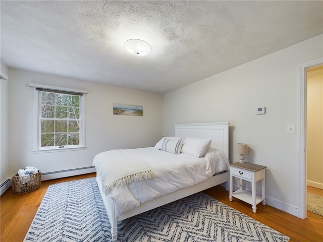 bedroom with a baseboard radiator, hardwood / wood-style floors, and a textured ceiling