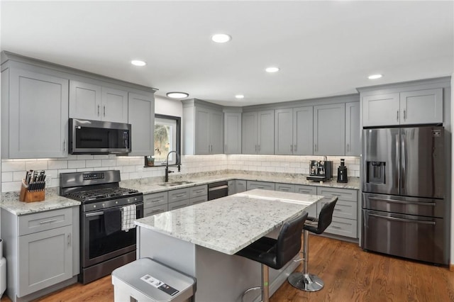 kitchen with sink, a breakfast bar area, a center island, stainless steel appliances, and light stone countertops