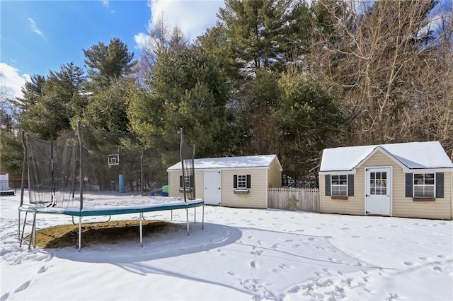 snowy yard featuring a trampoline and a shed