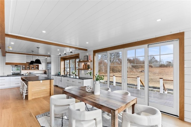 dining area featuring sink, light wood-type flooring, beam ceiling, and a wealth of natural light