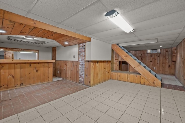 basement featuring wooden walls, tile patterned flooring, and a drop ceiling