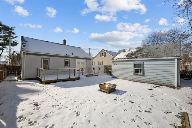 snow covered back of property with a wooden deck and a fire pit