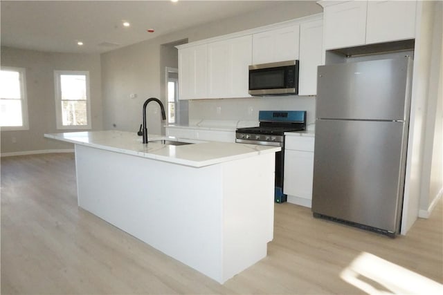 kitchen featuring sink, stainless steel appliances, white cabinets, a center island with sink, and light wood-type flooring