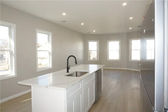 kitchen with sink, stainless steel dishwasher, an island with sink, light hardwood / wood-style floors, and white cabinets