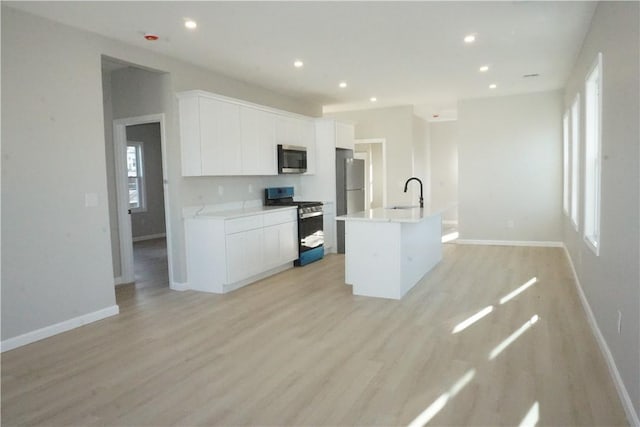 kitchen with appliances with stainless steel finishes, sink, a center island with sink, and white cabinets