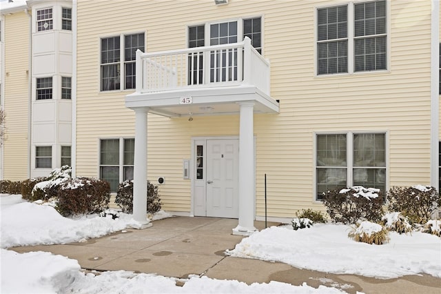 snow covered property entrance featuring a balcony