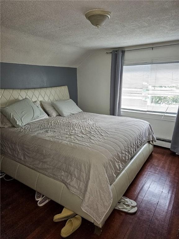 bedroom featuring lofted ceiling, dark hardwood / wood-style floors, a textured ceiling, and baseboard heating