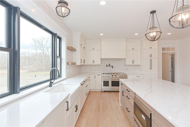 kitchen featuring appliances with stainless steel finishes, pendant lighting, sink, white cabinets, and light stone counters