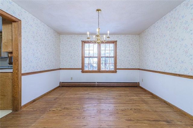 unfurnished room featuring a baseboard heating unit, hardwood / wood-style flooring, and a notable chandelier