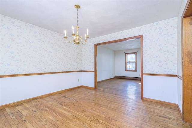 empty room with an inviting chandelier, a baseboard heating unit, and wood-type flooring