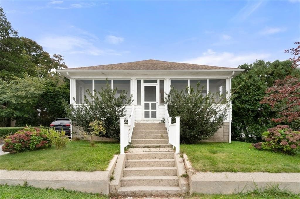 bungalow-style home with a front lawn, stairway, and a sunroom