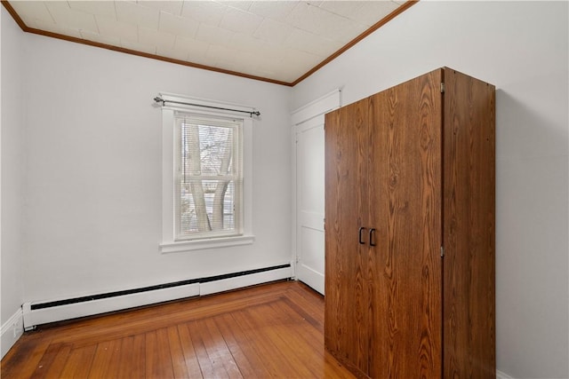 unfurnished bedroom featuring crown molding, wood-type flooring, and a baseboard heating unit