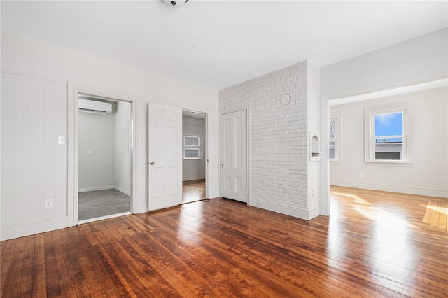 unfurnished bedroom featuring a wall mounted air conditioner, two closets, dark wood-type flooring, and brick wall