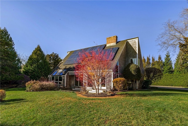 view of front of property with roof mounted solar panels, a chimney, and a front lawn