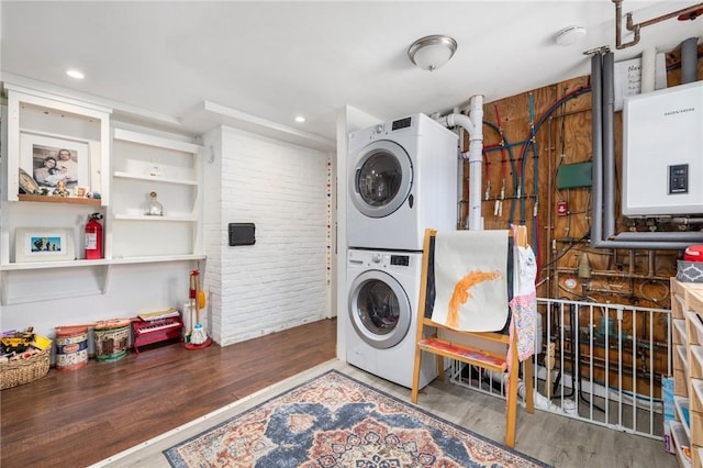 laundry room with stacked washer / drying machine, wood-type flooring, tankless water heater, and brick wall