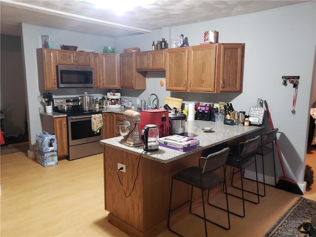 kitchen with sink, light wood-type flooring, appliances with stainless steel finishes, a kitchen breakfast bar, and kitchen peninsula