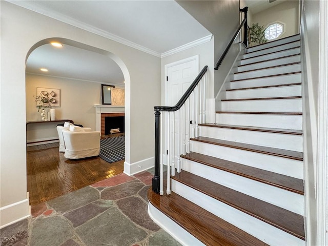 stairway featuring hardwood / wood-style flooring, ornamental molding, and a brick fireplace