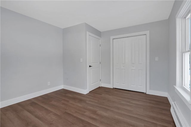 unfurnished bedroom featuring a baseboard heating unit, dark wood-type flooring, and a closet