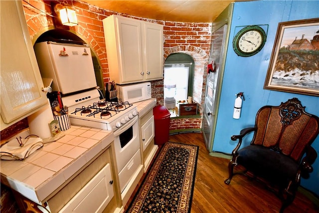 kitchen featuring brick wall, dark hardwood / wood-style floors, tile countertops, white cabinetry, and white appliances