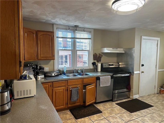 kitchen featuring stainless steel appliances, brown cabinetry, a sink, and under cabinet range hood