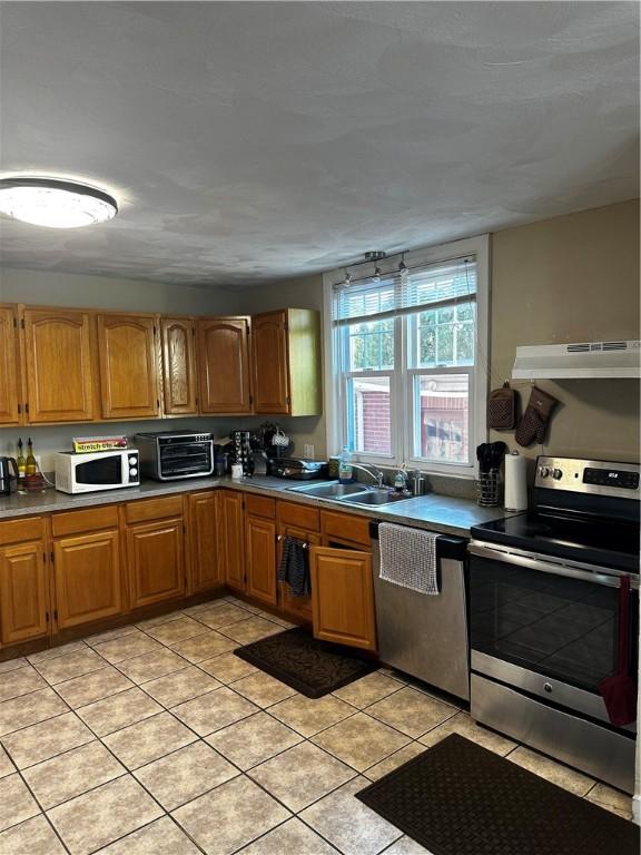 kitchen with a toaster, appliances with stainless steel finishes, brown cabinetry, a sink, and under cabinet range hood