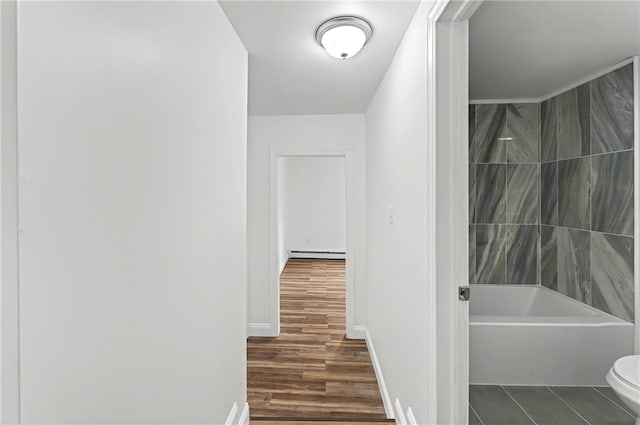 interior space with baseboard heating, toilet, tiled shower / bath combo, and hardwood / wood-style floors