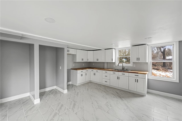 kitchen with tasteful backsplash, sink, white cabinets, and butcher block countertops