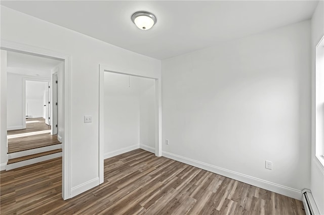 unfurnished bedroom with a baseboard heating unit, dark wood-type flooring, and a closet