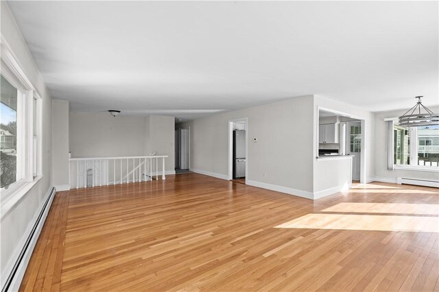 unfurnished living room with baseboard heating, baseboards, light wood-style floors, and a baseboard radiator