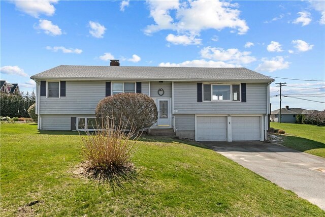 raised ranch with a chimney, driveway, an attached garage, entry steps, and a front yard