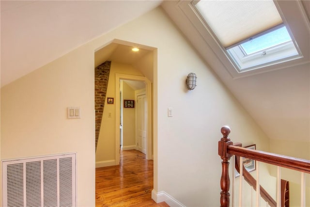 corridor with vaulted ceiling with skylight and light wood-type flooring