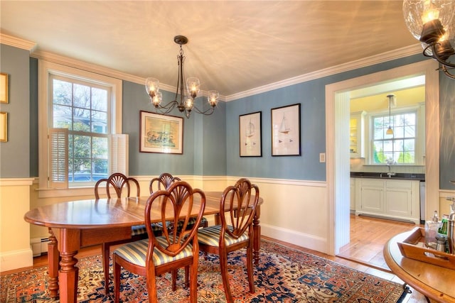 dining space with a baseboard heating unit, ornamental molding, a healthy amount of sunlight, and light wood-type flooring