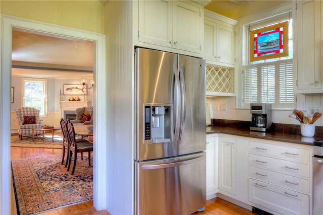 kitchen with white cabinetry, stainless steel refrigerator with ice dispenser, light hardwood / wood-style floors, ornamental molding, and dark stone counters