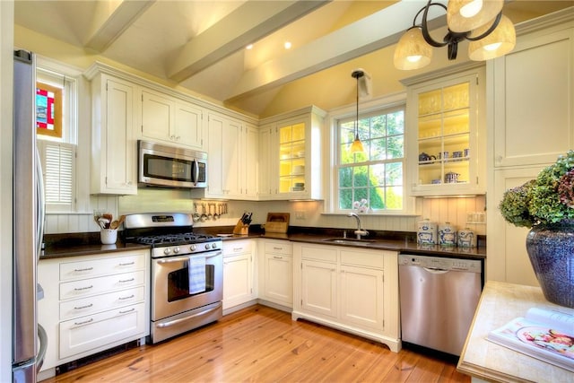 kitchen featuring appliances with stainless steel finishes, pendant lighting, white cabinetry, sink, and light hardwood / wood-style flooring