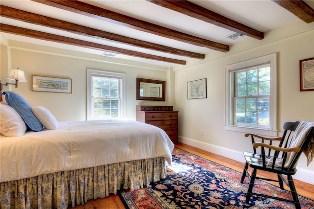 bedroom with beamed ceiling, wood-type flooring, and multiple windows