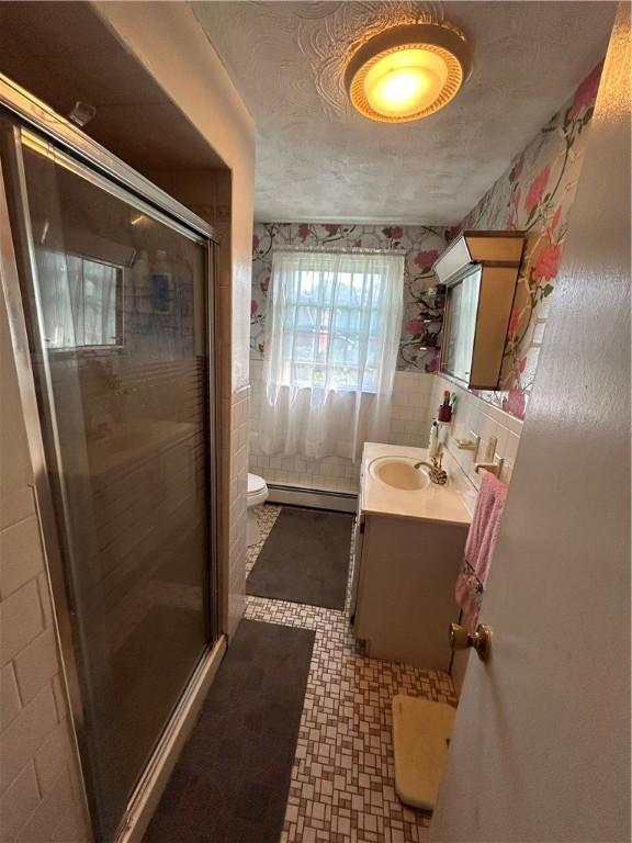 bathroom with baseboard heating, tile walls, vanity, a textured ceiling, and toilet