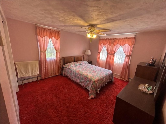 carpeted bedroom with multiple windows, ceiling fan, a baseboard heating unit, and a textured ceiling