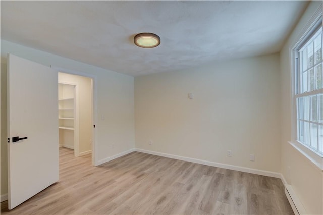 spare room featuring a baseboard heating unit and light wood-type flooring