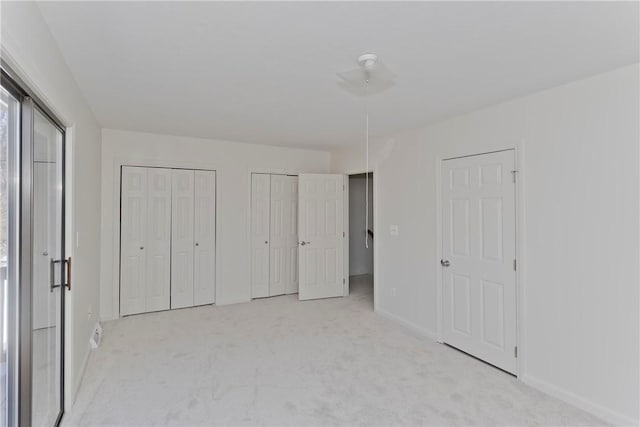 unfurnished bedroom with light colored carpet, baseboards, and two closets