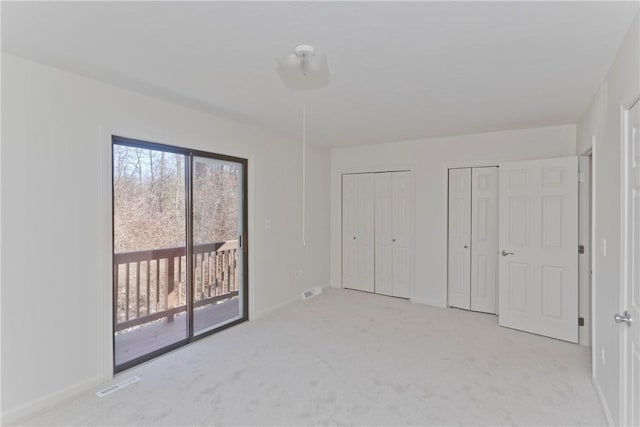 unfurnished bedroom featuring carpet floors, visible vents, baseboards, multiple closets, and access to outside