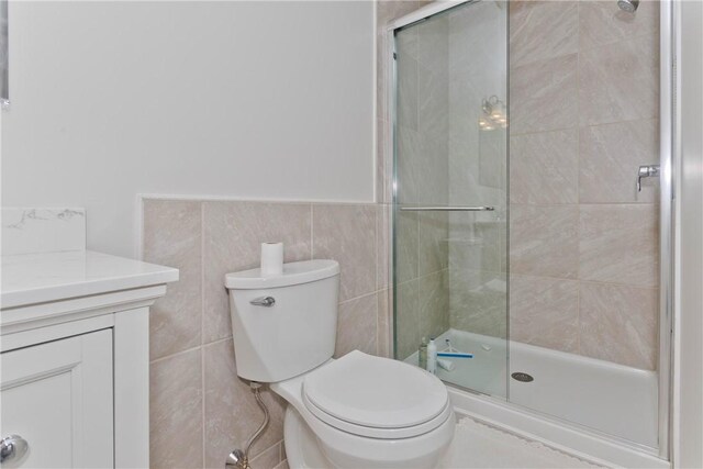 full bath featuring toilet, a wainscoted wall, vanity, tile walls, and a shower stall