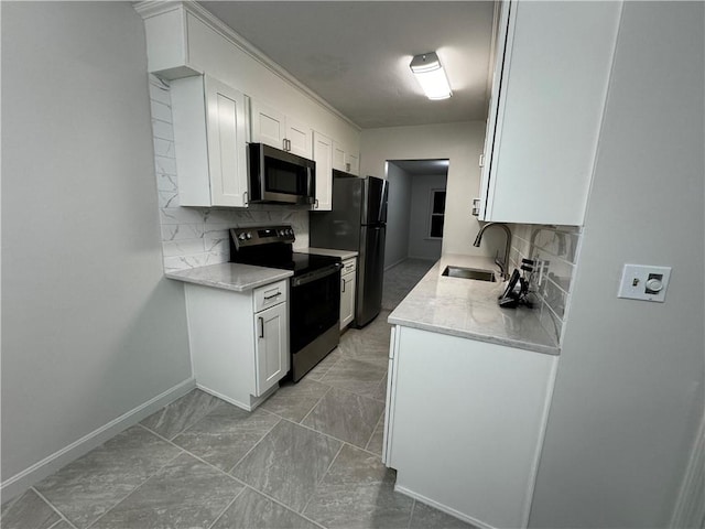 kitchen featuring light countertops, appliances with stainless steel finishes, white cabinets, a sink, and baseboards