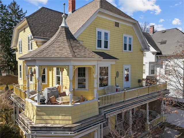 rear view of house featuring a shingled roof and a chimney