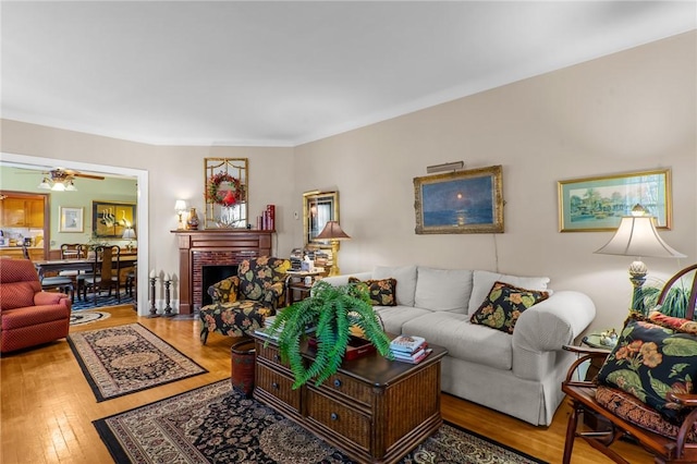 living area featuring hardwood / wood-style flooring, ceiling fan, and a brick fireplace