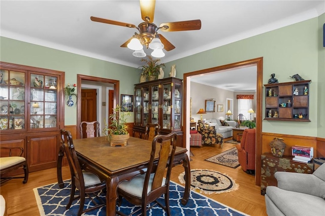 dining area featuring a wainscoted wall, ceiling fan, and light wood finished floors