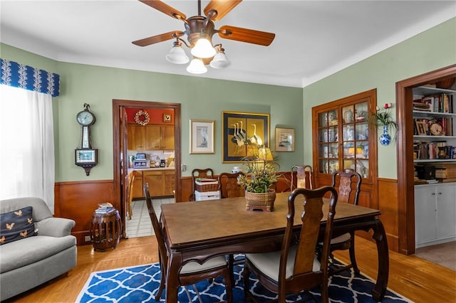 dining space featuring a ceiling fan, light wood-type flooring, and wainscoting